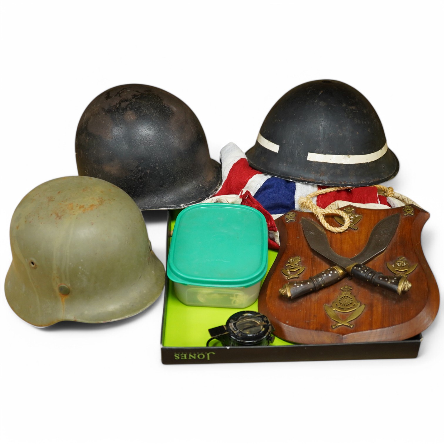 A collection of military items, including a U.S. Army helmet, an M42 helmet, a WWII British Home Front helmet, a Union flag 96cm x 60cm, a compass, a Kukri display shield, and a box of military cap badges, buttons, etc.